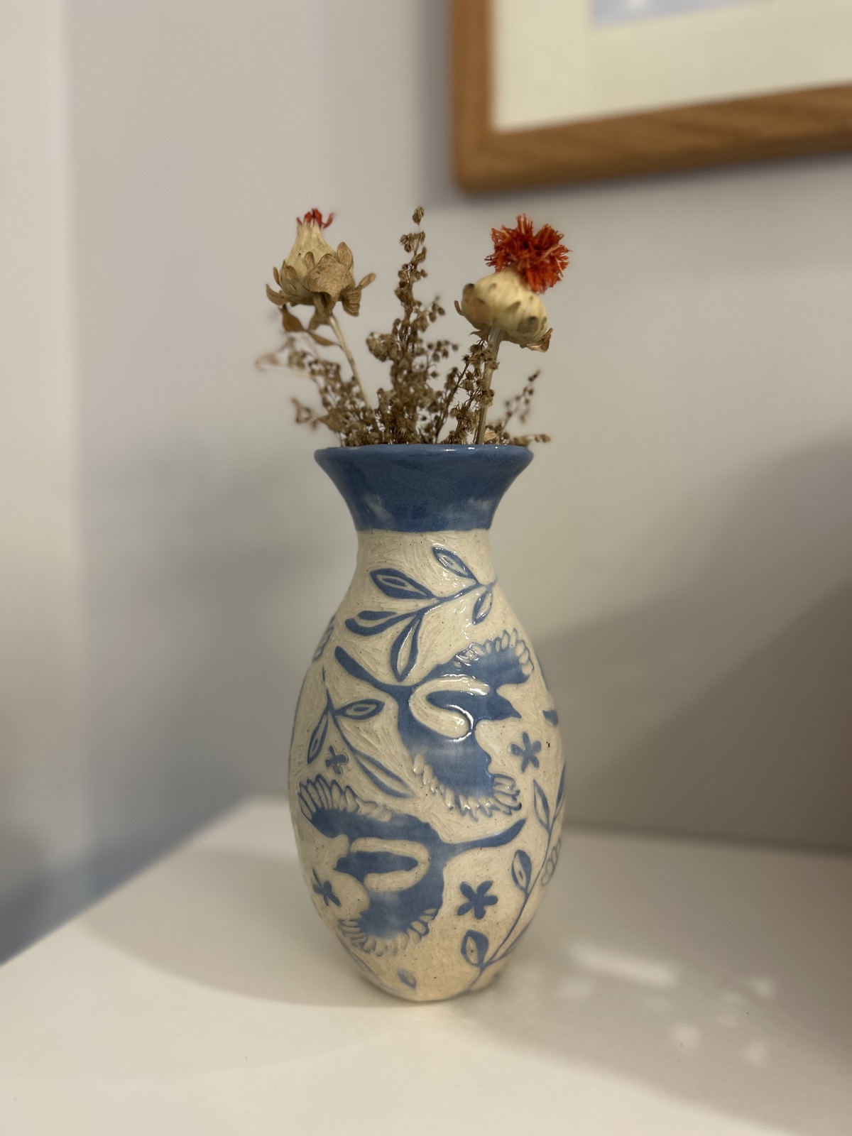 Blue-and-cream ceramic vase with carved birds and leaves, holding dried flowers
