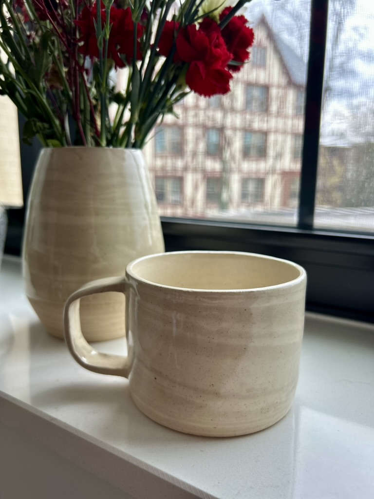 Cream ceramic mug and vase on a windowsill