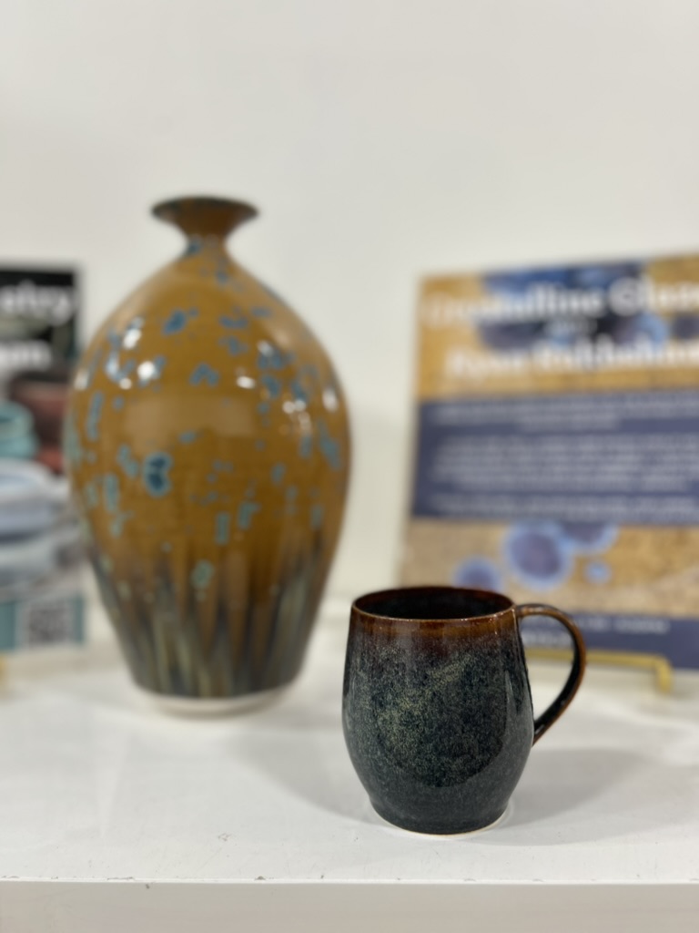 Dark glazed mug in front of an amber vase